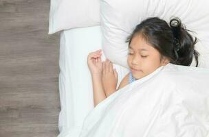 mignonne peu asiatique fille sommeil sur lit dans le chambre à coucher. photo