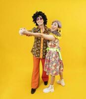 asiatique hippie couple robe dans Années 80 ancien mode avec coloré rétro Vêtements tandis que dansant ensemble isolé sur Jaune Contexte pour fantaisie tenue fête et pop culture concept photo