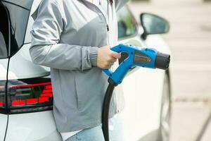 Jeune affaires femme Ravitaillement sa électrique voiture à une ev mise en charge gare. concept de écologiquement amical véhicule. électrique voiture concept. vert en voyageant. photo