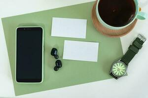 tondu coup de Masculin style, intelligent téléphone sur vert moderne Bureau bureau avec affaires carte, thé tasse, montre. photo