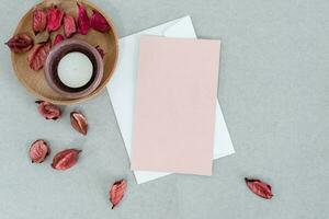 vide rose carte avec blanc enveloppe, bougie et pétales, sur gris Contexte. photo