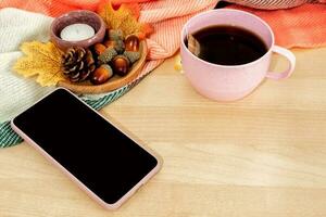 thé tasse, intelligent téléphone , l'automne feuilles sur en bois Contexte. photo