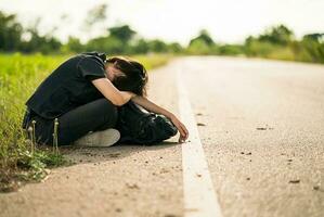 femme assise avec un sac à dos faisant de l'auto-stop le long d'une route dans la campagne photo