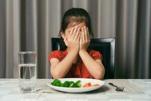 peu mignonne enfant fille refusant à manger en bonne santé des légumes. les enfants faire ne pas comme à manger des légumes. photo