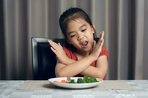 peu mignonne enfant fille refusant à manger en bonne santé des légumes. les enfants faire ne pas comme à manger des légumes. photo