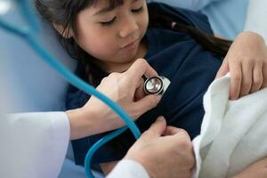 femme asiatique médecin pédiatre tenir stéthoscope pour examen une petite fille patiente et sacré poumons cardiaques d'enfant, bon médecin de famille visitant un enfant à la maison, soins de santé et médecine pour le concept de l'enfance. photo