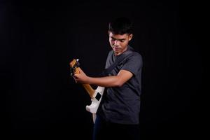 Jeune homme en veste de cuir noir avec guitare électrique sur fond noir en studio
