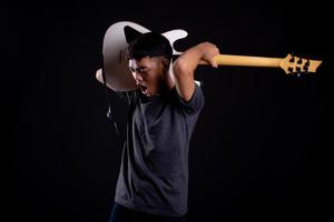 Jeune homme en veste de cuir noir avec guitare électrique sur fond noir en studio photo