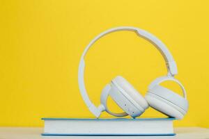 concept de livre audio avec un casque blanc moderne et un livre à couverture rigide sur fond jaune. écouter un livre. photo
