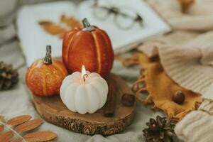 confortable l'automne décor - brûlant bougie forme de citrouille et Orange décor citrouilles sur en bois planche sur lit avec ouvert livre, chaud chandail, l'automne feuilles photo