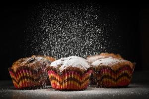 le cuisinier saupoudre les muffins de sucre en poudre sur fond noir photo
