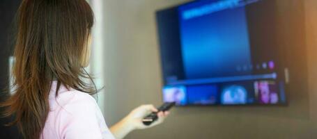 main de femme à l'aide de la télécommande pour régler la télévision intelligente à l'intérieur de la chambre moderne à la maison photo