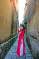 content femme portant ao dai vietnamien robe et chapeau, voyageur tourisme à salut un ancien ville dans central vietnam. point de repère et populaire pour touristique attractions. vietnam et sud-est Voyage concept photo