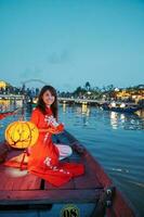 femme portant ao dai vietnamien robe, voyageur tourisme bateau balade et flottant papier lanterne à salut un ancien ville. point de repère pour touristique attractions.vietnam et sud-est Voyage concept photo