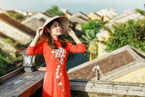 content femme portant ao dai vietnamien robe, voyageur tourisme vue à toit à salut un ancien ville dans vietnam. point de repère et populaire pour touristique attractions. vietnam et sud-est Voyage concept photo