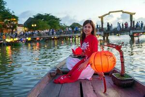 femme portant ao dai vietnamien robe, voyageur tourisme bateau balade et flottant papier lanterne à salut un ancien ville. point de repère pour touristique attractions.vietnam et sud-est Voyage concept photo