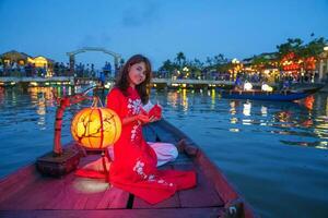 femme portant ao dai vietnamien robe, voyageur tourisme bateau balade et flottant papier lanterne à salut un ancien ville. point de repère pour touristique attractions.vietnam et sud-est Voyage concept photo