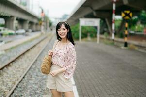 magnifique asiatique Jeune femme voyageur avec tissage panier permanent à côté de chemin de fer train station dans Bangkok. périple voyage mode de vie, monde Voyage explorateur ou Asie été tourisme concept. photo