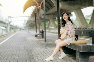 Jeune asiatique femme voyageur avec tissage panier attendre pour train dans train gare. périple voyage mode de vie, monde Voyage explorateur ou Asie été tourisme concept. photo
