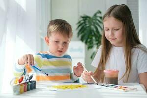 frère et sœur dessiner une image avec des peintures sur une pièce de papier. les enfants sont apprentissage à dessiner. Accueil la créativité. photo