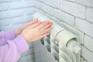 le enfant mains chaud leur mains près le chauffage radiateur. économie gaz dans le chauffage saison. photo