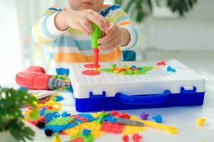 peu garçon en jouant ensemble avec une Tournevis et une percer, et des vis et les pièces . le enfant pièces constructeur avec une jouet percer à développer imagination et moteur compétences. éducatif logique jouets pour les enfants. photo