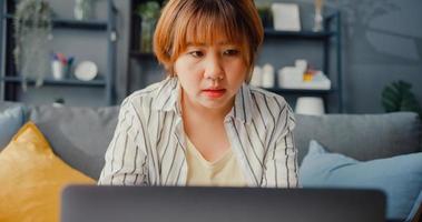 femme asiatique indépendante vêtements décontractés à l'aide d'un ordinateur portable apprentissage en ligne dans le salon de la maison photo