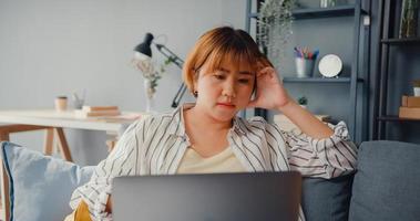 une dame asiatique indépendante a mal à la tête alors qu'elle est assise sur un canapé avec un ordinateur portable en ligne, apprenez dans le salon de la maison photo