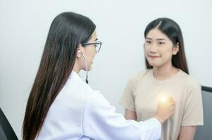 asiatique femelle médecin dans uniforme en portant une stéthoscope et en utilisant il à mesure le cœur taux de un asiatique femelle patient avec cœur maladie photo