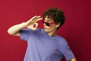 portrait de une Jeune frisé homme main gestes cœur en forme de des lunettes posant isolé Contexte photo