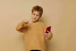 de bonne humeur garçon avec rouge téléphone dans mains posant beige Contexte photo