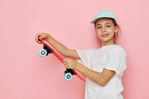 portrait de content souriant enfant fille casquette dans blanc T-shirt planche à roulette rose Contexte photo