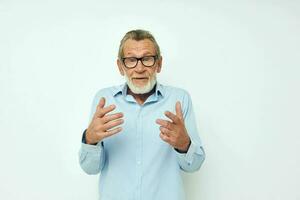 Sénior aux cheveux gris homme dans bleu chemises gestes avec le sien mains lumière Contexte photo