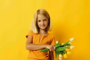 peu fille avec blond cheveux avec une bouquet de Jaune fleurs sur une Jaune Contexte photo