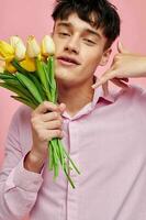 Beau gars dans une rose chemise avec une bouquet de fleurs faire des gestes avec le sien mains isolé Contexte inchangé photo