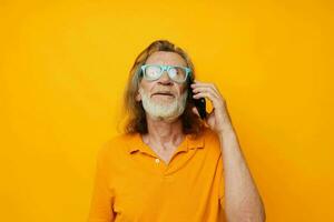vieux homme dans Jaune t-shirts et des lunettes parlant sur le téléphone isolé Contexte photo