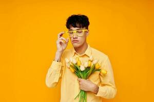 jolie homme dans Jaune des lunettes avec une bouquet de fleurs Jaune Contexte inchangé photo