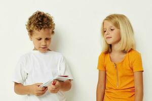 garçon et fille amusement dans coloré t-shirts avec une bloc-notes isolé Contexte inchangé photo