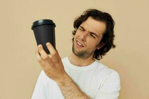 de bonne humeur homme dans une blanc T-shirt avec une noir verre dans main beige Contexte photo