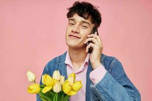 Jeune gars dans une denim veste avec une bouquet de fleurs parlant sur le téléphone rose Contexte photo