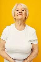 portrait de un vieux amical femme dans décontractée T-shirt gestes avec le sien mains fermer émotions photo