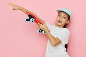 portrait de content souriant enfant fille casquette dans blanc T-shirt planche à roulette rose Contexte photo