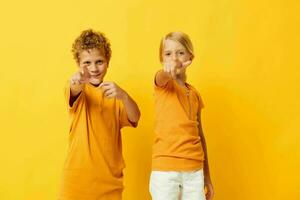 mignonne élégant des gamins dans Jaune t-shirts permanent côté par côté enfance émotions isolé Contexte inchangé photo