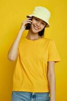 attrayant femme dans une Jaune chapeau jeunesse style décontractée parlant sur le téléphone isolé Contexte photo