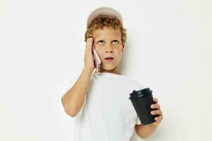 mignonne garçon dans une blanc T-shirt casquette avec une téléphone dans une verre avec une boisson mode de vie inchangé photo