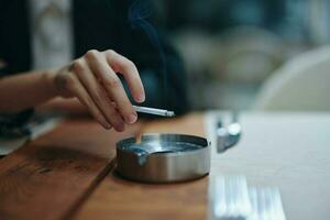 une femme avec une cigarette dans sa mains secoue le cendres dans un cendrier, fermer photo