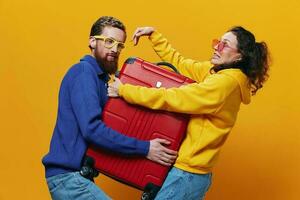 femme et homme souriant, les valises dans main avec Jaune et rouge valise souriant joyeusement et courbé, Jaune arrière-plan, Aller sur une voyage, famille vacances voyage, jeunes mariés. photo