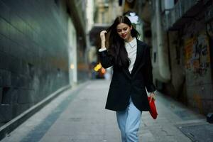 mode femme sourire avec les dents et amusement touristique dans élégant vêtements dans veste et rouge béret en marchant vers le bas étroit ville rue en volant cheveux, voyage, français style, cinématique couleur, rétro style. photo