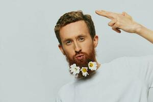 portrait de une marrant homme dans une blanc T-shirt avec fleurs marguerites dans le sien barbe sur une blanc isolé arrière-plan, copie lieu. vacances concept et toutes nos félicitations. photo