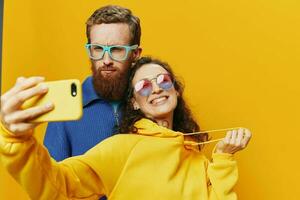 femme et homme marrant couple avec Téléphone (s main social la mise en réseau et la communication courbé faire selfies sourire amusant, sur Jaune Contexte. le concept de réel famille des relations, indépendants, travail en ligne. photo